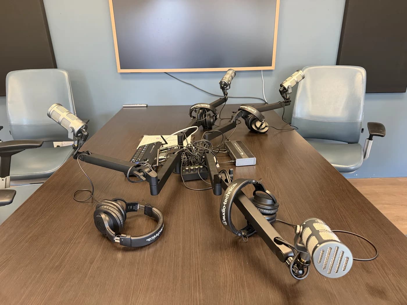 Podcast studio table with microphones, headphones, audio console, and two guest chairs.